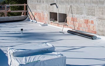 Flat rooftop under construction with insulation panels, rolled waterproof membrane, and exposed brick walls in sunlight.